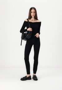 Off-shoulder svart topp, kombinert med svarte tettsittende bukser og svarte slip-on sko. Modellen holder en rund svart håndveske.