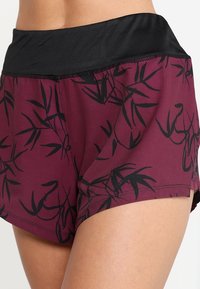 Burgundy shorts with black bamboo pattern, featuring a wide black waistband, soft fabric, and a curved hem for mobility.
