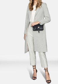 Světle šedý vlněný kabát s přesným střihem, doplněný texturovanými světle šedými kalhotami. Černé sandály s k�řížovým páskem a malá černá taška dotvářejí vzhled.