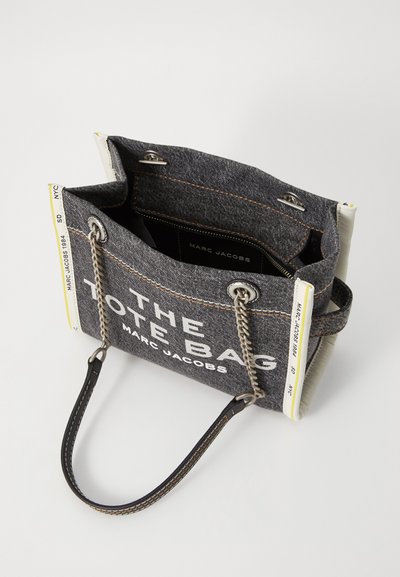 Sac fourre-tout en denim gris avec des accents contrastants jaunes et blancs. Doté d'une chaîne et d'une sangle en cuir, d'une poche intérieure et d'un texte audacieux.
