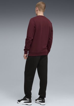 Mørkerød sweatshirt med en rund halsudskæring og ribbede manchetter, parret med sorte sweatpants. Accent lynlåse på bukserne og markante sneakers.