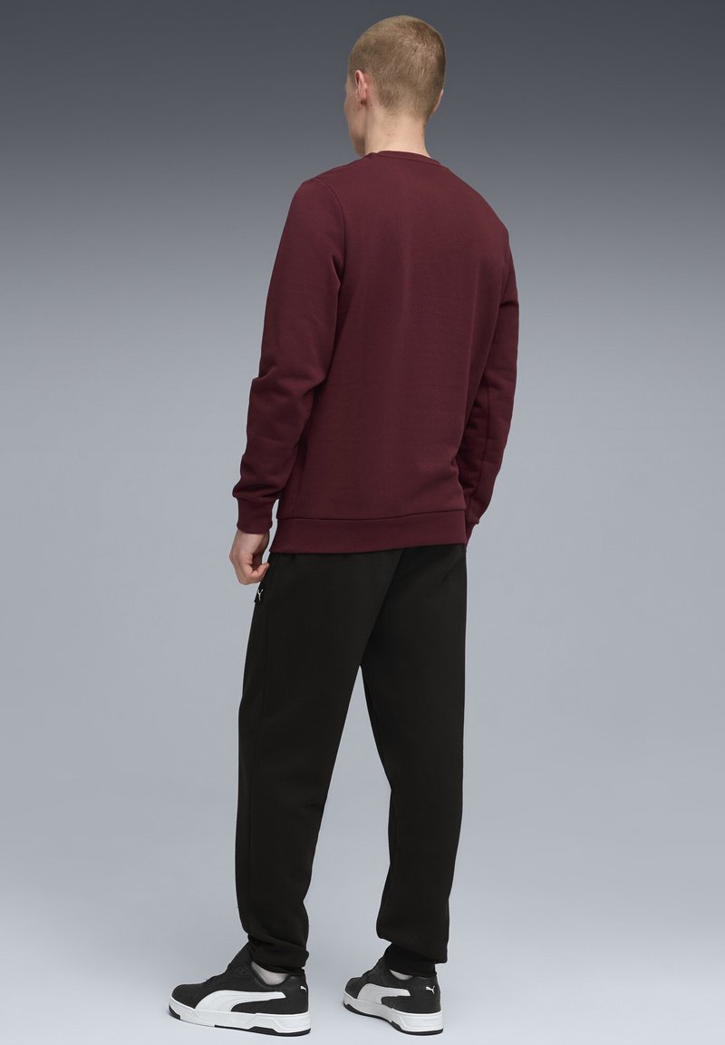 Bordeauxfarbiges Sweatshirt mit Rundhalsausschnitt und gerippten Bündchen, kombiniert mit schwarzen Jogginghosen. Akzentreißverschlüsse an den Hosen und auffällige Sneakers.