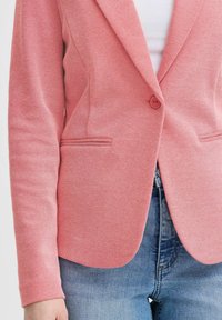 Rosa texturerad blazer med en enkel knappstängning, snedskurna slag och två framfickor, matchad med ljus denimjeans.