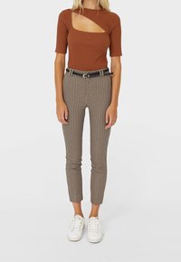 Haut marron côtelé à manches courtes avec une découpe, associé à un pantalon à carreaux taille haute et des baskets blanches. Une ceinture noire souligne la taille.