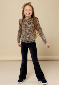 Lange mouw top met luipaardprint in bruin en zwart, gecombineerd met marineblauwe flared corduroybroek. Model draagt donkere instappers en een bruine haarband.