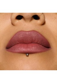 Lápiz labial mate color malva aplicado en labios llenos, con un piercing plateado centrado debajo. Textura suave con un sutil degradado de color.