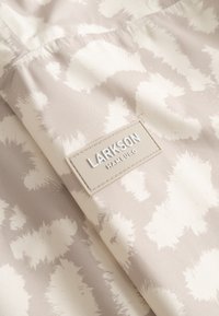 Tessuto beige e bianco con motivo astratto a macchie si piega per mostrare un'etichetta rettangolare Larkson Hamburg cucita.