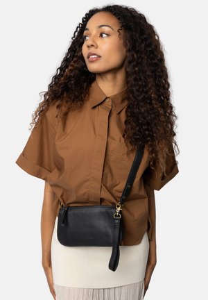 Borsa a tracolla nera in pelle con cerniera, dotata di una tracolla staccabile e hardware dorato, posizionata su una gonna chiara.