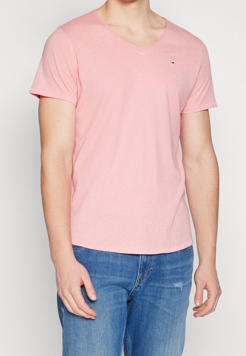 T-shirt en coton rose à col en V, manches courtes, coupe décontractée, avec un petit logo sur la poitrine. Associé à un jean en denim bleu.