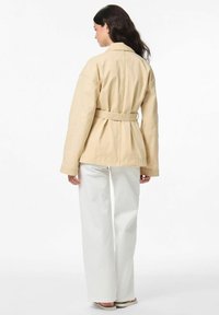 Veste en coton beige à ceinture, avec un col classique, une coupe décontractée et des manches longues, associée à un pantalon large blanc et des sandales.