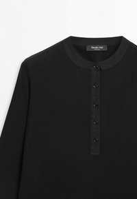 Chemise noire à manches longues avec col rond et cinq boutons noirs sur la patte de boutonnage avant, en tissu doux.