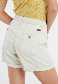 Pantaloni corti beige chiaro con vita elasticizzata, due tasche posteriori, cuciture a contrasto e un piccolo etichetta del marchio sul retro.