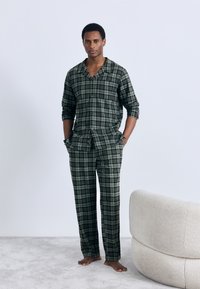 Set di pigiama a quadri verdi con camicia abbottonata e pantaloni con vita elastica, realizzato in tessuto morbido, caratterizzato da una tasca sul petto e maniche risvoltate.