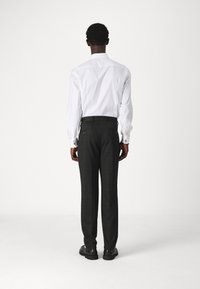Chemise blanche à manches longues avec des poignets, associée à un pantalon à carreaux gris foncé. Des chaussures noires soulignent le look professionnel.