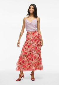 Gonna maxi floreale rosa con ruffles a strati, abbinata a una canotta in satin viola chiaro e sandali con tacco alto rossi e con cinturini.