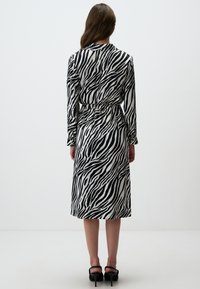 Lang slim fit jurk in een zwart-wit zebra patroon, met lange mouwen, een taille met riem en een rechte zoom. Ontworpen voor een slanke silhouet.
