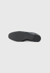Black leather shoe with a smooth finish, rounded toe, and a low, textured rubber sole. Features visible stitching along the edges.
