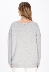 Grauer gestrickter Pullover mit weitem Halsausschnitt, überschnittenen Schultern und lockerer Passform. Weiche Textur und gerippte Bündchen mit Logo auf der Rückseite.
