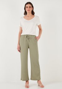 Pantalons larges légers de couleur vert olive avec un tissu texturé et une taille à cordon réglable, associés à un t-shirt blanc à col en V.