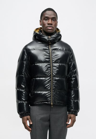 Sort pufferjakke med blank finish, lynlås og elastiske manchetter. Har hætte med kontrasterende mønster og foer.