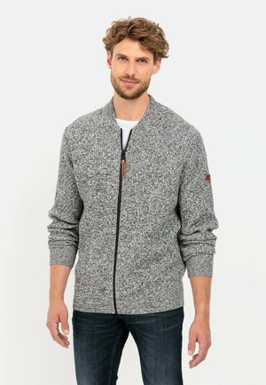 Grauer, strukturierter Pullover mit Reißverschluss, gerippten Bündchen und Saum. Verfügt über ein dezentes Logo auf dem linken Ärmel. Wird über einem weißen T-Shirt getragen.