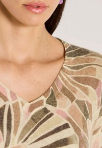 Frau trägt einen mehrfarbigen, gemusterten V-Ausschnitt-Pullover und konzentriert sich auf den Hals, das Schlüsselbein und die Lippen mit glänzendem rosa Lippenstift.