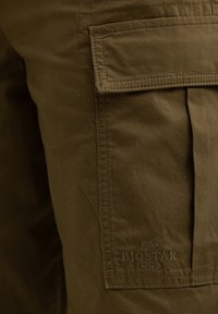 Olivne zelene cargo hlače s aplikacijskim žepom in šivi. Vključuje embosirano logotip "BIG STAR 1979" na tkanini. Trajen material.
