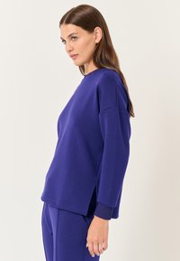 Felpa viola dal taglio rilassato, con spacchi laterali, scollatura rotonda e polsini a coste, realizzata in un tessuto morbido e leggero.