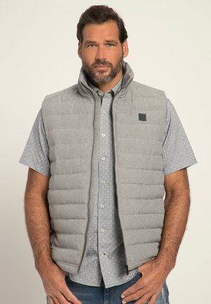 Chaleco acolchado gris con cuello alto, tejido texturizado, costuras horizontales y un parche de logo. Llevado sobre una camisa de botones azul claro con estampado.