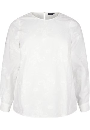 Blusa bianca con maniche lunghe, scollo rotondo e una sottile texture floreale. Presenta un'apertura a forma di chiave sul retro con una cerniera. Materiale in cotone morbido.