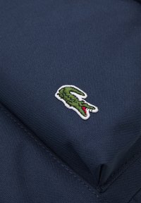 Sac en textile bleu marine arborant un logo de crocodile brodé en vert et rouge, avec une surface texturée et des détails de couture soignés.