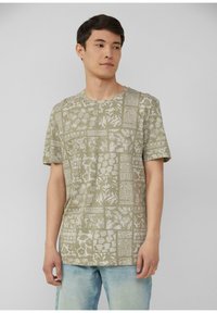 Groen T-shirt met korte mouwen, versierd met een wit botanisch patroon, ronde halslijn en een ontspannen pasvorm, gecombineerd met lichtblauwe jeans.