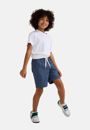 T-shirt blanc à manches courtes associé à un short bleu avec une taille élastique et un cordon de serrage. Enfant portant des baskets blanches avec des accents colorés.