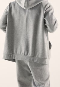 Grauer Kapuzenpullover und passende Jogginghose aus weichem Stoff. Der Hoodie verfügt über eine Kängurutasche und einen gerippten Saum; die Hose hat eine Gesäßtasche.