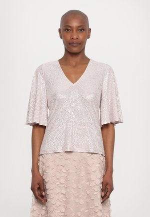 Pale pink, short-sleeve top with a V-neck, featuring textured fabric and a shimmering finish. Paired with a floral embroidered skirt.