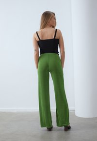 Top noir sans manches et pantalon vert taille haute à jambes larges. Texture lisse et couleur vive avec une silhouette fluide. Design minimaliste.