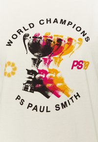 Camiseta blanca con un estampado gráfico abstracto de copas de trofeo en negro, rosa y amarillo. El texto dice "CAMPEONES DEL MUNDO" y "PS PAUL SMITH."