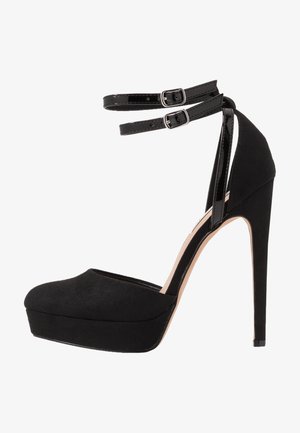 Black high-heeled shoe with a suede finish, round toe, platform sole, and dual ankle straps. Glossy accents complement the matte texture.