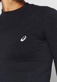 Schwarzes, langärmeliges Sportoberteil mit strukturierten Akzenten, das eine taillierte Passform aufweist und ein kleines weißes Logo auf der Brust hat. Glattes, dehnbares Material.