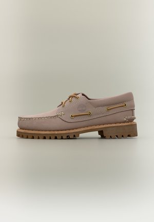 Zapato náutico de cuero beige con suela texturizada, detalles de cordones y logo de Timberland en el lateral, mostrado sobre un fondo neutro.