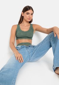 Bralette en dentelle vert foncé, avec des bords festonnés et une texture douce, associé à un jean large bleu clair avec une finition délavée.