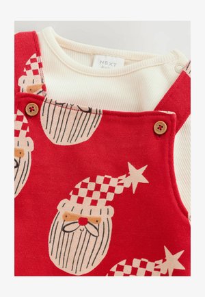 Raudoni medvilniniai kombinezonai su kalėdų senelio veidu ir žvaigždutėmis, po kuriais yra balto audinio ilgomis rankovėmis marškiniai. Mediniai mygtukų akcentai ant petnešų.