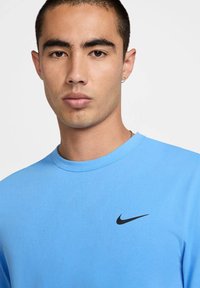 T-shirt Nike bleu avec un col rond. Présente un logo noir subtil sur la poitrine. Texture lisse et coupe décontractée.