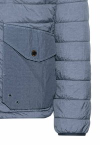 Polstret jakke i lyseblå stof med en struktureret overflade. Har en stor skråtstillet lomme og trykknaplukning, samt ventilationshuller.