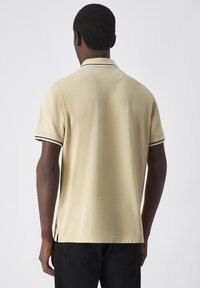 Korte mouw polo-shirt in beige, met een contrasterende zwarte kraag en mouwafwerking, gemaakt van een gladde stof met een comfortabele pasvorm.
