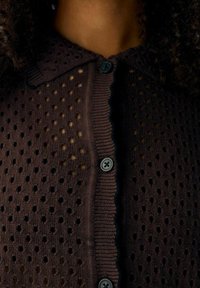 Cardigan en maille marron à texture ajourée, avec un col à revers et trois boutons foncés, bordé d'un bord festonné contrastant.