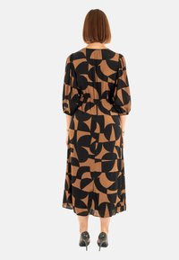 Vestido negro y marrón con un patrón, mangas globo, cintura ceñida y largo hasta la mitad de la pantorrilla. La tela parece ligera y fluida.