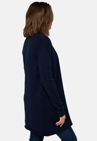 Cardigan long bleu marine en tissu tricoté, avec une coupe décontractée, un devant ouvert et des poches latérales, doté de poignets et d'un ourlet côtelés.