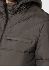 Harmaa pehmeä takki, jossa on tekstuuri, hupullinen, vinosti ommeltu ja vetoketjullinen rintatasku. Metalliosat näkyvillä.