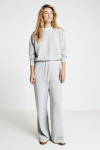 Sweat-shirt gris et pantalon large en tissu doux. Le pantalon comporte une taille à cordon de serrage et des poignets côtelés aux chevilles.